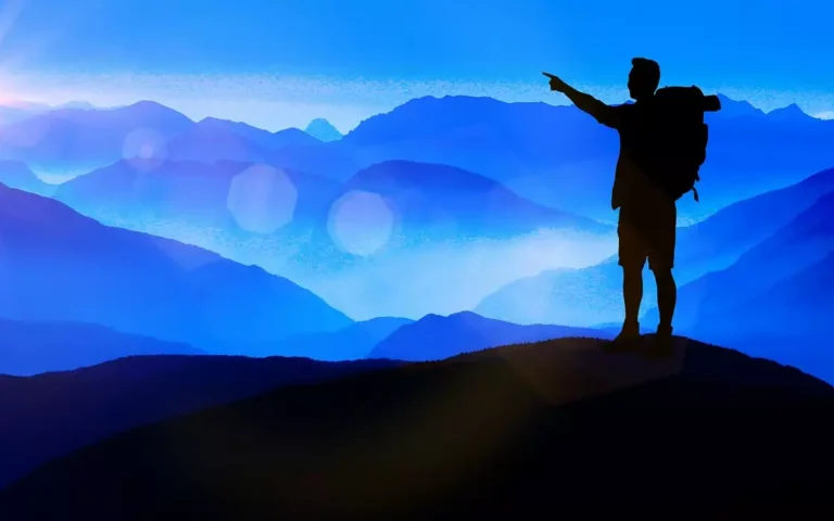 Male backpacker has hiked to top of mountain, sun is setting, he is pointing to distant sunset.