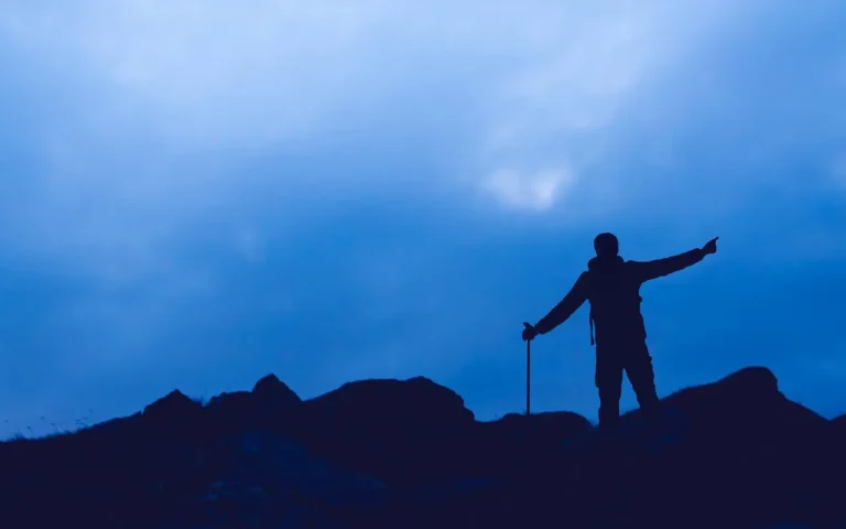 Hiker at top of mountain ridge pointing into the distance.
